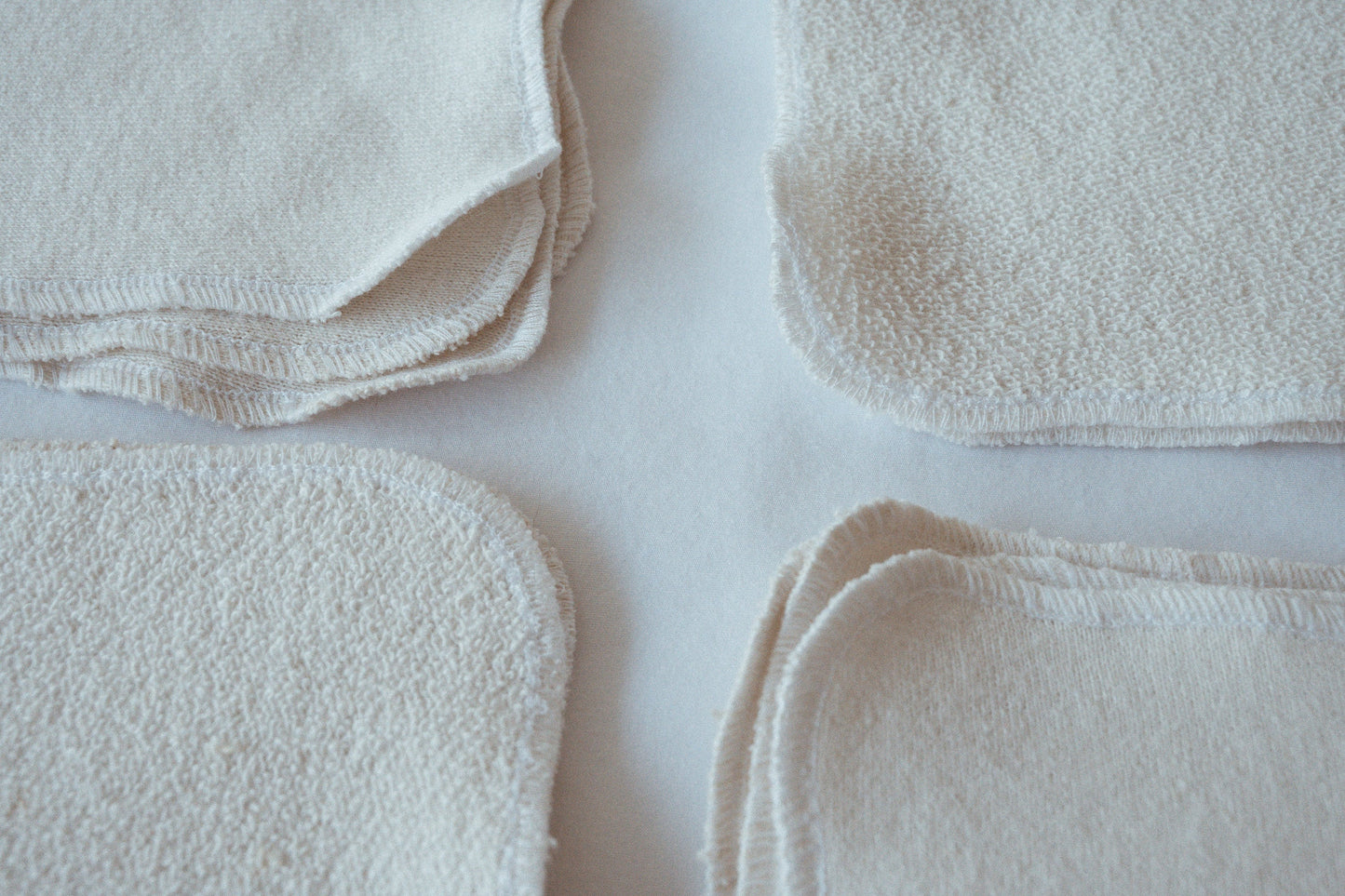 Close-up of four stacks of ORGANIC WASHCLOTHS by cabane childrenswear, handmade in Vancouver from organic cotton. Each set includes four soft, white, square cloths with rounded corners arranged on a white surface.