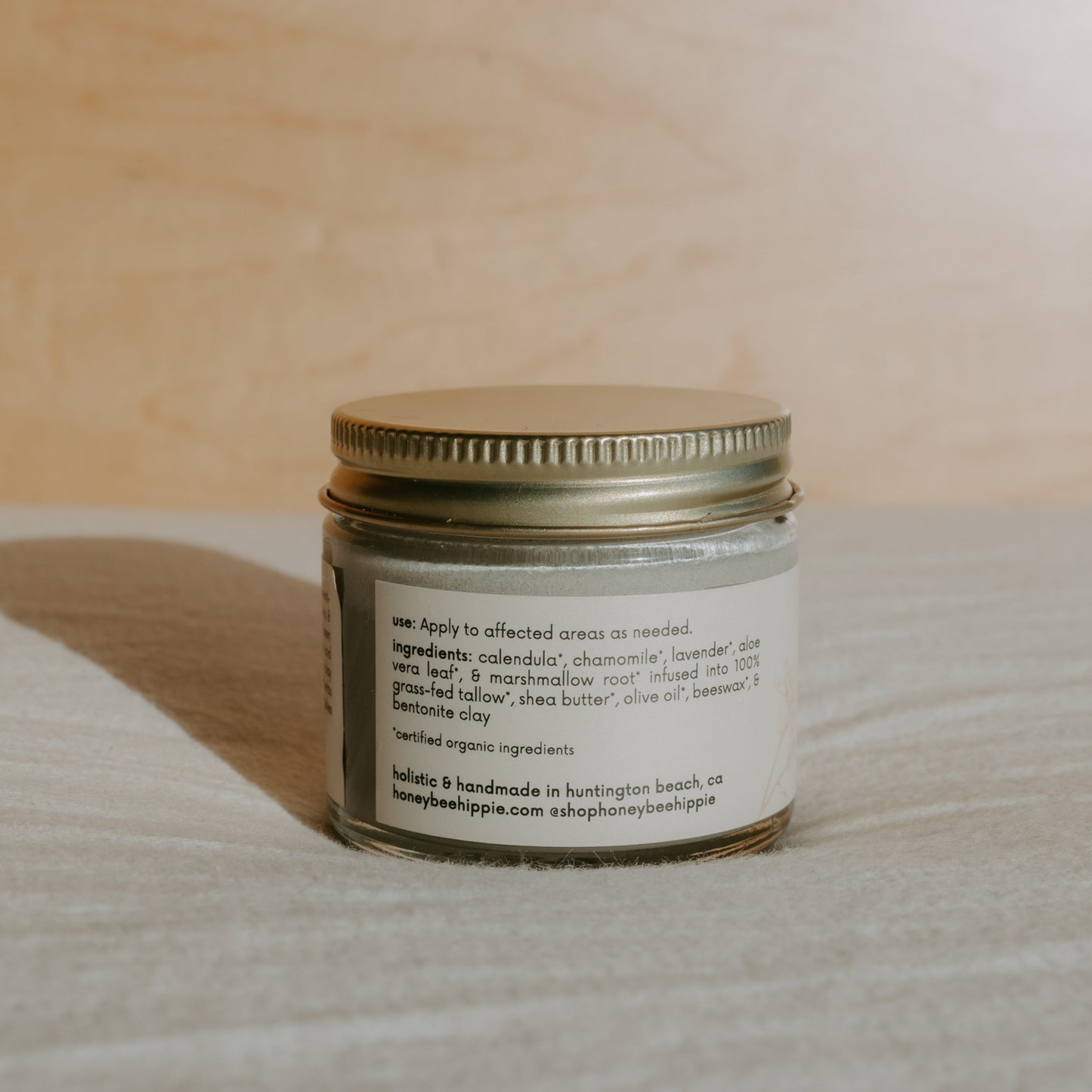 A jar of miracle mud from Honeybee Hippie has a metallic lid and a beige label with usage instructions. This Huntington Beach, CA tallow-based balm is enriched with calendula and chamomile for natural skincare, including diaper rash relief. Visit the brand's website for more info.