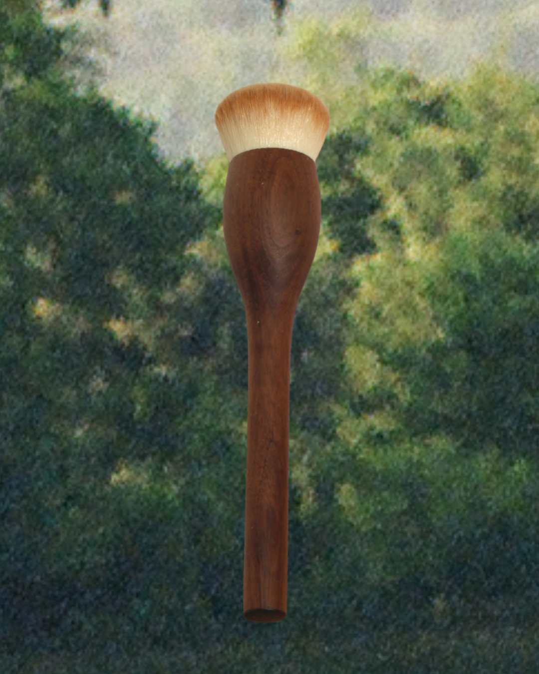 The & Tread Well Dry Shampoo Brush, featuring a walnut wooden handle and soft, rounded bristles, is centered against a blurred green and beige background evocative of foliage—ideal for refreshing natural hair.