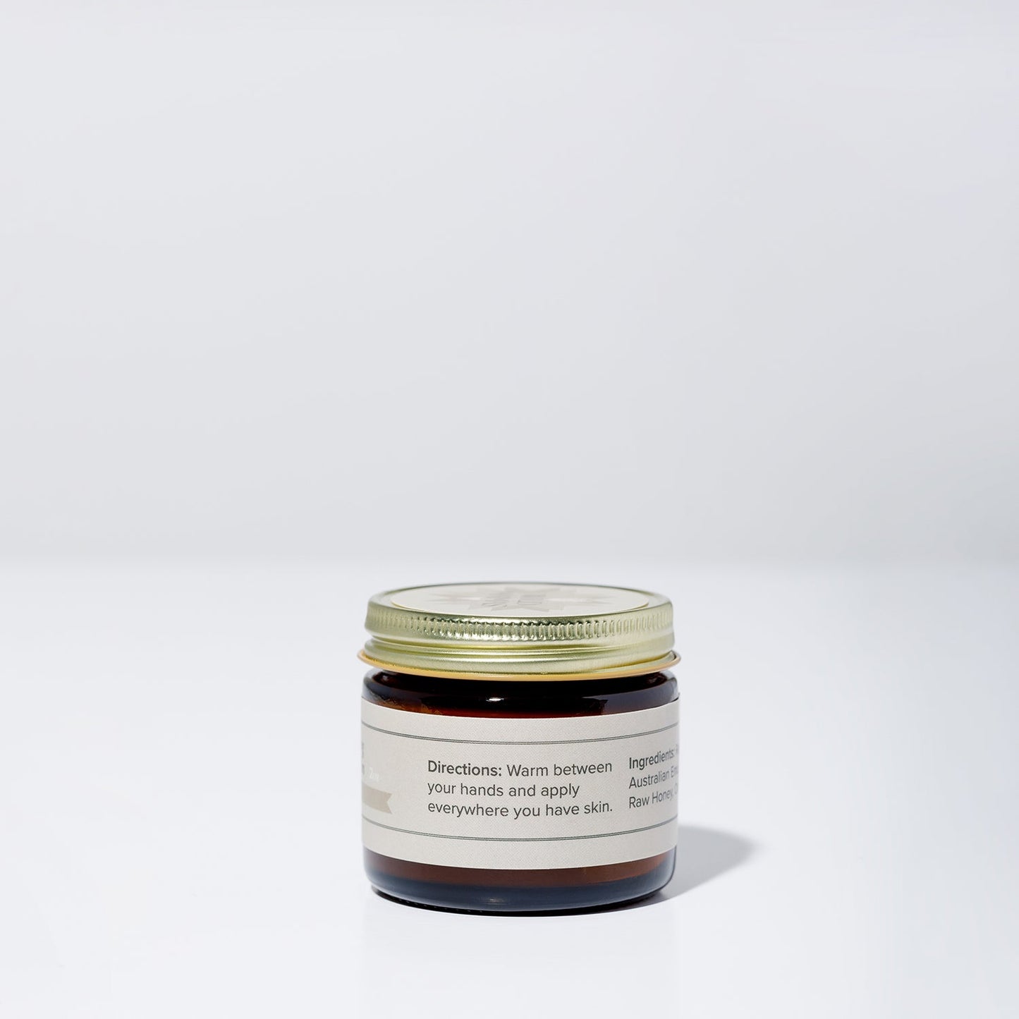 A small amber jar with a gold lid sits on a white surface, labeled “Wildly Nourishing Bison Tallow Balm - Raw Honey” by WildMamas, crafted from bison tallow and thoughtfully sourced regenerative ingredients.