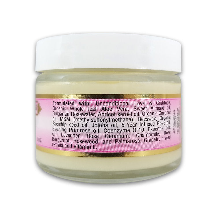 A clear glass jar with a white lid displays Simply Divine Botanicals' Crème de Rose Radiant Hydrating Moisturizer, featuring a pink and gold label. Key ingredients: aloe vera, sweet almond oil, rosewater, apricot kernel oil, beeswax, essential oils, and vitamin E.