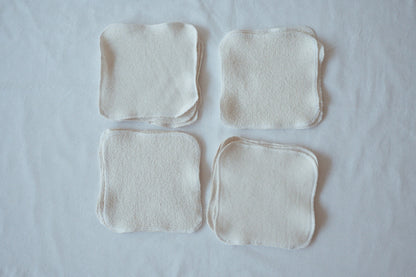 A set of four square ORGANIC WASHCLOTHS by cabane childrenswear—crafted from organic cotton and hemp french terry—are arranged in a grid on white fabric, each with rounded corners and visible textured material.