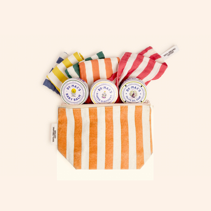 The Dr. Max's Newborn Gift Box includes a zippered pouch with orange and white stripes, three tins of baby balm diaper ointment and lotion, plus three rolled cloths in blue, yellow, and red stripes—perfect for newborns.
