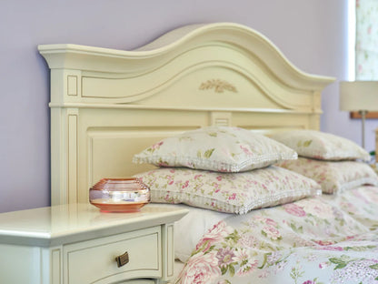 A bedroom featuring the Rosalin by Somavedic USA—a cream headboard, floral bedding, plush pillows, and a glass candle holder on a matching nightstand—creates an atmosphere ideal for supporting circadian rhythms.