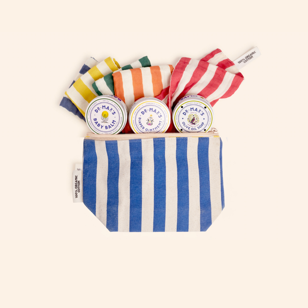 The Dr. Max's Newborn Gift Box features a blue and white striped pouch with three tins of baby balm diaper ointment and three colorful cloths in yellow, green, and red, set against a light background.