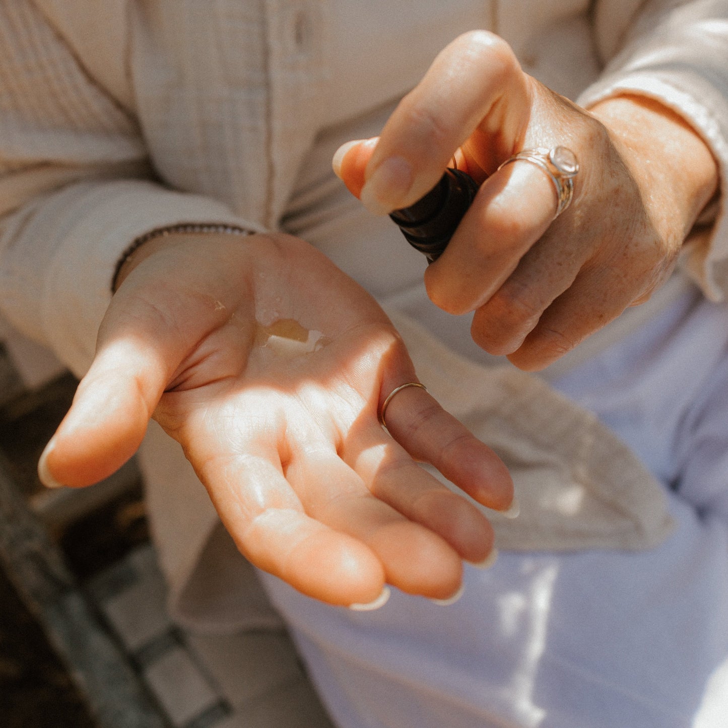 A person dispenses Honeybee Hippie’s saffron serum onto their open palm from a small bottle, wearing light clothing and rings, in natural light.