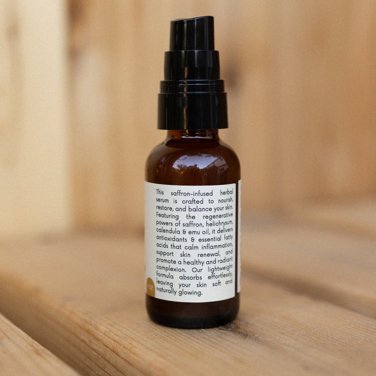 A small amber bottle with a black pump from Honeybee Hippie rests on wood. Its label highlights the saffron serum as antioxidant-rich, formulated to nourish, restore, and balance skin.