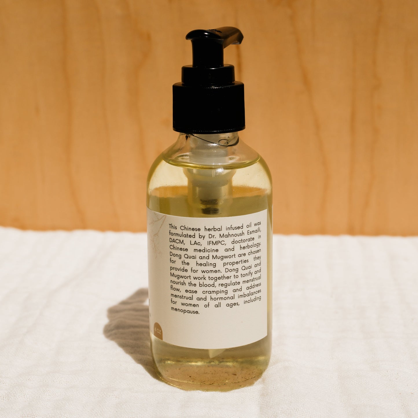 A clear glass bottle with a black pump stores a light-colored liquid. Labeled Honeybee Hippie's "herbal infused castor oil packs," it emphasizes Chinese herbs and herbal oil, promoting women's holistic health and natural healing through various life stages.