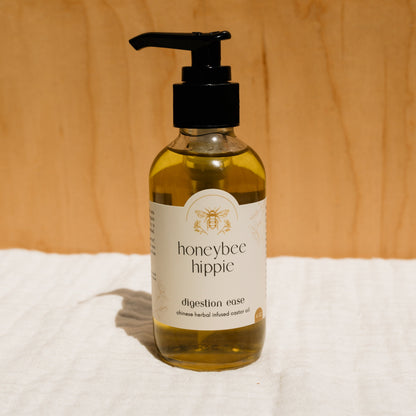 A bottle of Honeybee Hippie herbal infused castor oil packs is on a white cloth against a wooden background, embodying holistic health. Perfect for natural remedy enthusiasts, it features a pump dispenser and a charming bee illustration on the label.