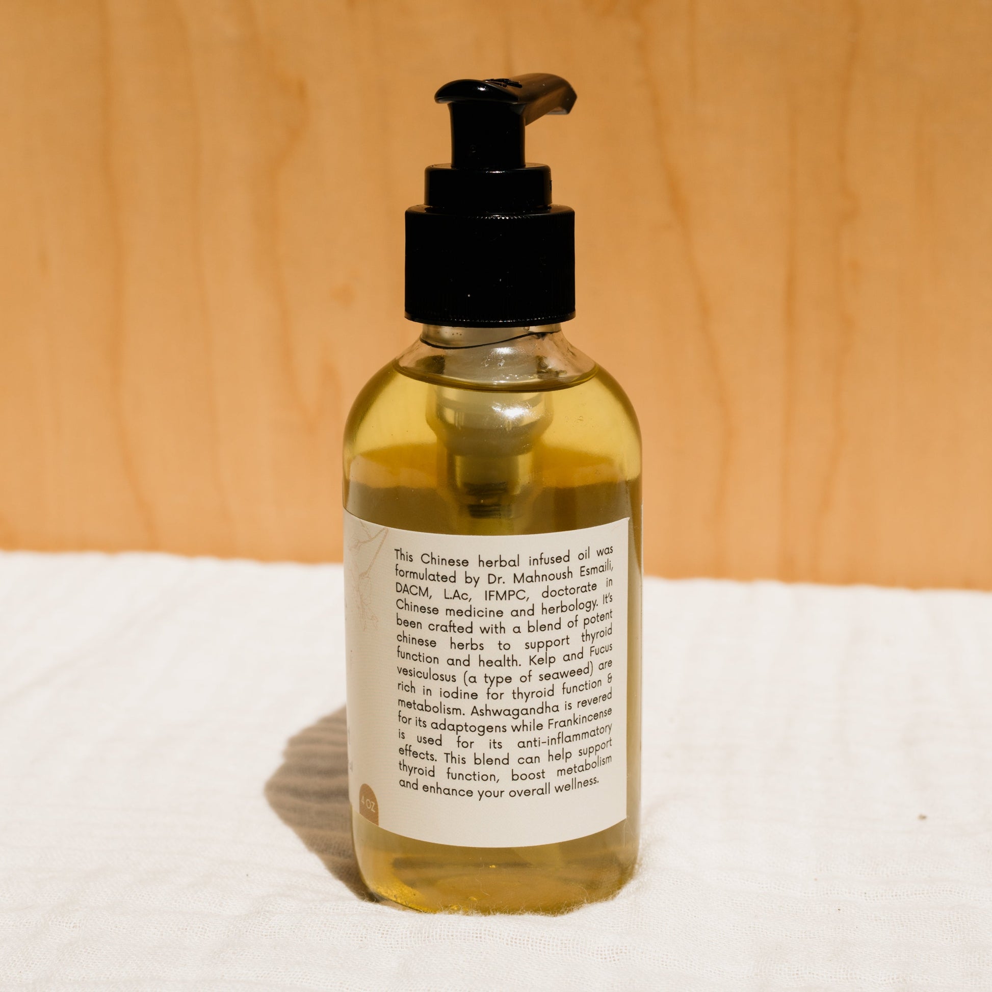 A bottle of Honeybee Hippie's herbal infused castor oil packs with a black pump dispenser stands against a light background, featuring a partially visible label hinting at holistic health benefits.