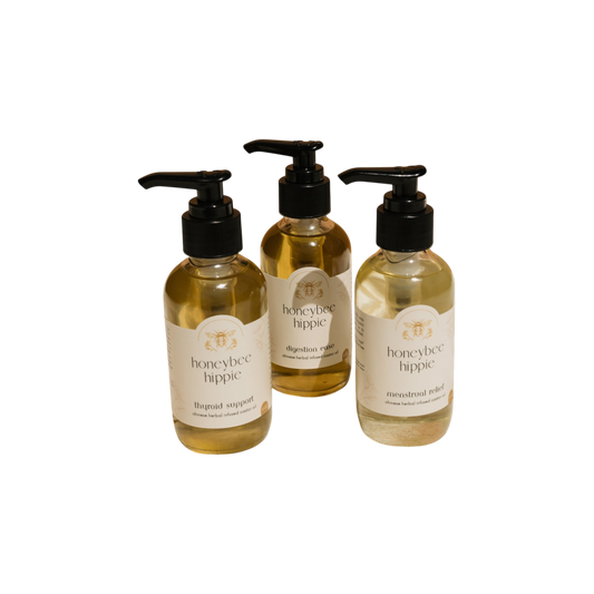 Three bottles of Honeybee Hippie herbal-infused castor oil packs, featuring labels that say "thyroid support," "digestion support," and "menstrual relief," are arranged in a triangle against a black background, highlighting their holistic health benefits.