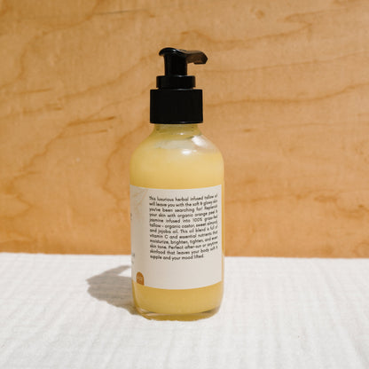 A bottle with a black pump, labeled "California Sunshine - Tallow Oil" by Honeybee Hippie, sits on a textured white surface. Its non-comedogenic oil boasts organic orange peel essence, with the yellow liquid contrasting beautifully against the beige wood-texture background.