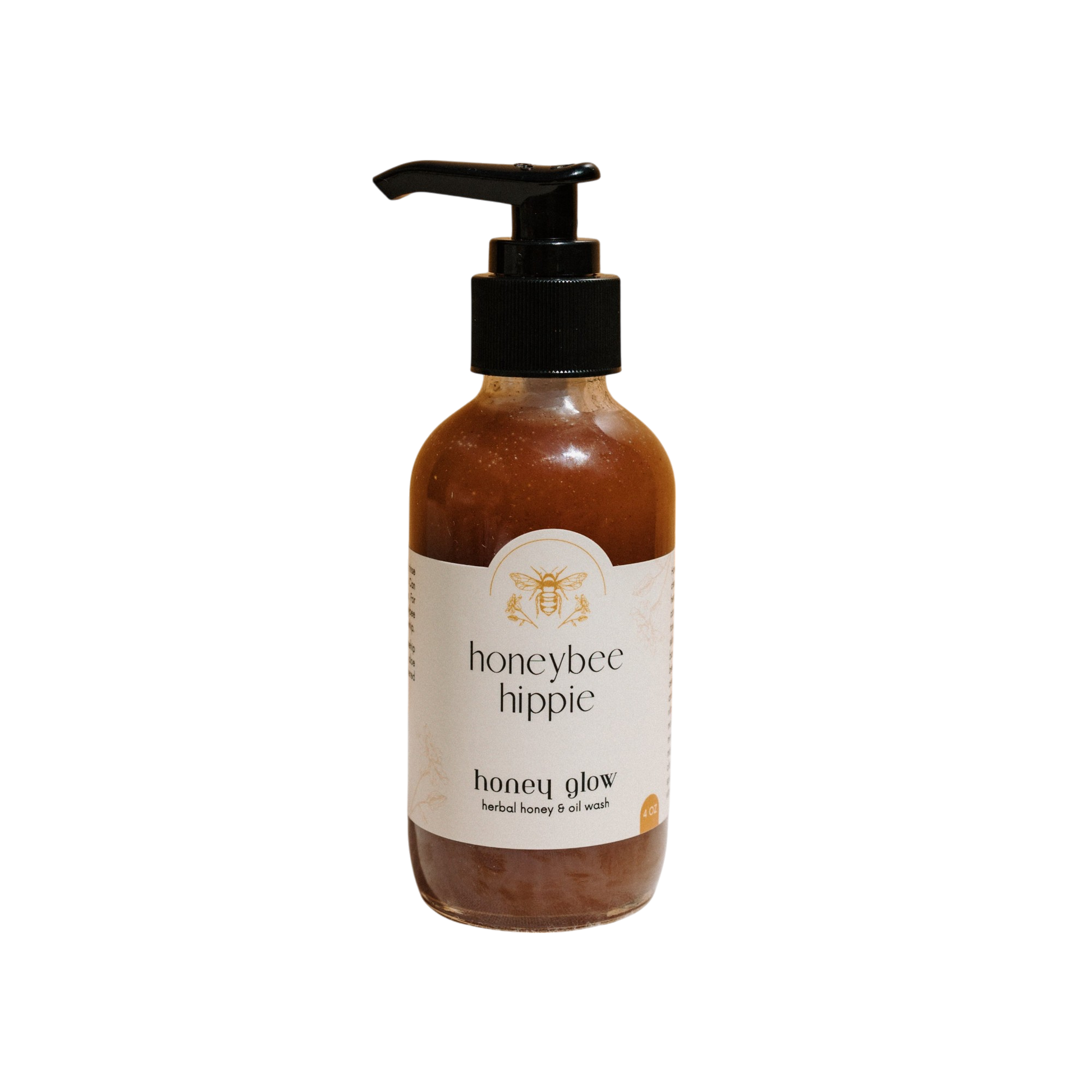 A bottle of Honeybee Hippie's "Honey Glow" herbal honey & oil wash with a pump top features a bee illustration on a white label, highlighting raw honey and organic oils. The amber gel contrasts beautifully against the black backdrop.