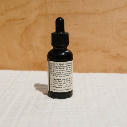 A small brown bottle of Honeybee Hippie's hair & beard oil with a black dropper cap rests on a beige surface. The label, highlighting frizz control benefits and ingredients, blends seamlessly with the warm wooden background.