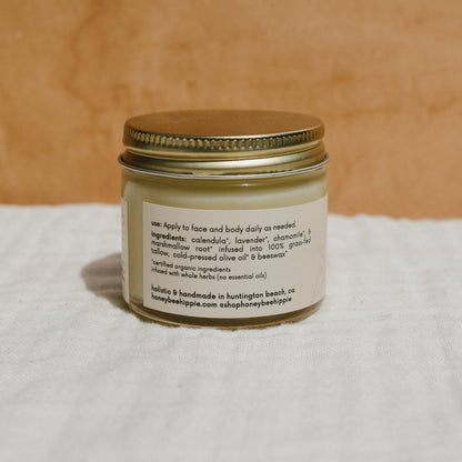 The Honeybee Hippie natural mama tallow balm is a holistic skincare cream with a gold lid. It features calendula, lavender, chamomile, olive oil, grass-fed tallow, and organic herbs. Handmade in Huntington Beach, CA, it's ideal for sensitive skin.