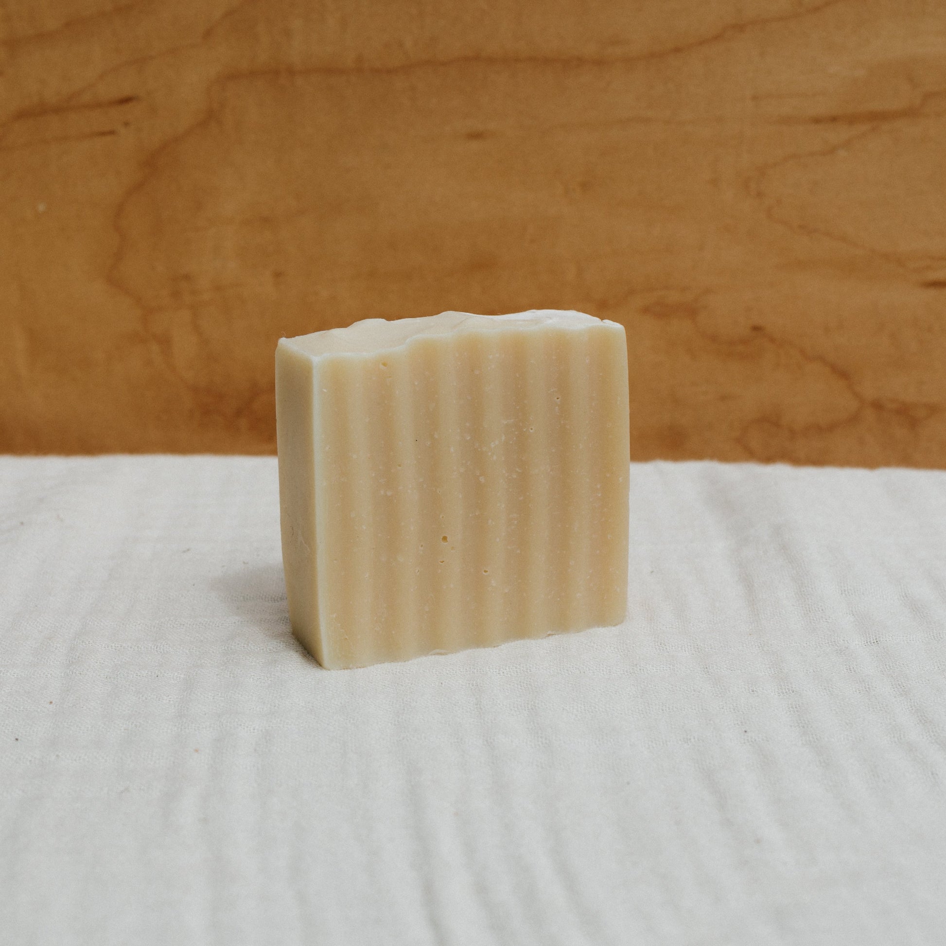 The Honeybee Hippie's handcrafted Honeybee Tallow Soap Bar, with its ridged texture, elegantly stands on a white fabric, while a wooden background enhances its natural allure.