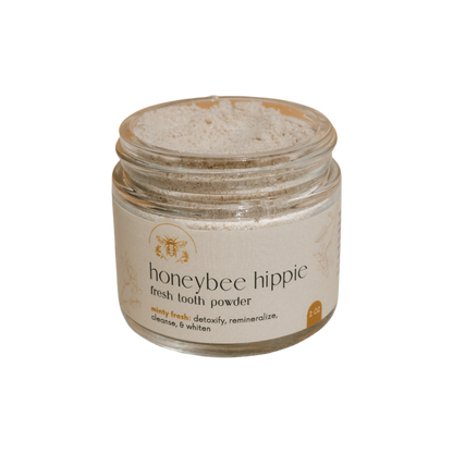 Honeybee Hippie's fresh tooth powder detoxifies, whitens, and remineralizes teeth while delivering minty freshness. A partially filled jar holds this revitalizing formulation designed to cleanse your smile.