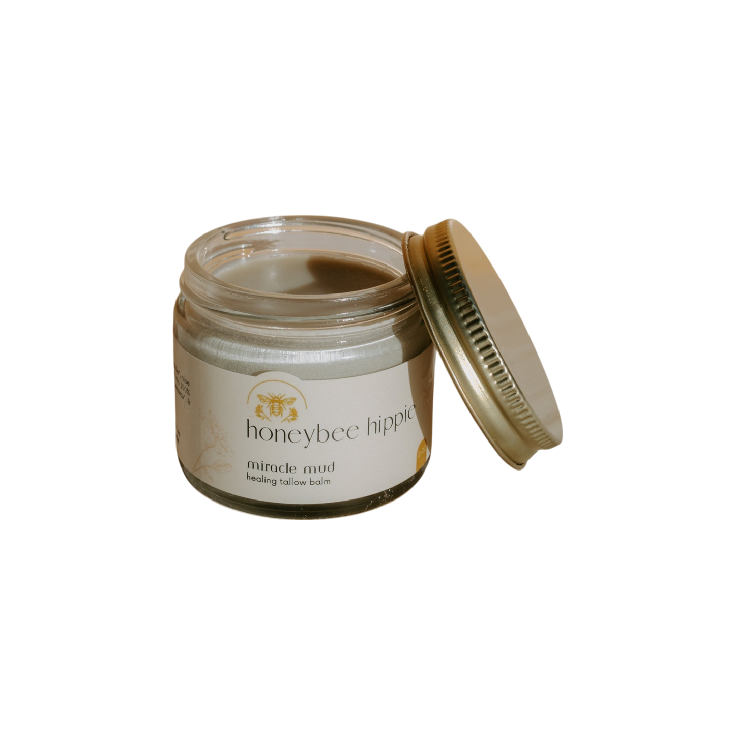 A jar of Honeybee Hippie's "miracle mud" tallow balm, ideal for skincare and diaper rash relief, has a slightly open gold lid. Its label showcases a bee illustration and text, set against a black background.