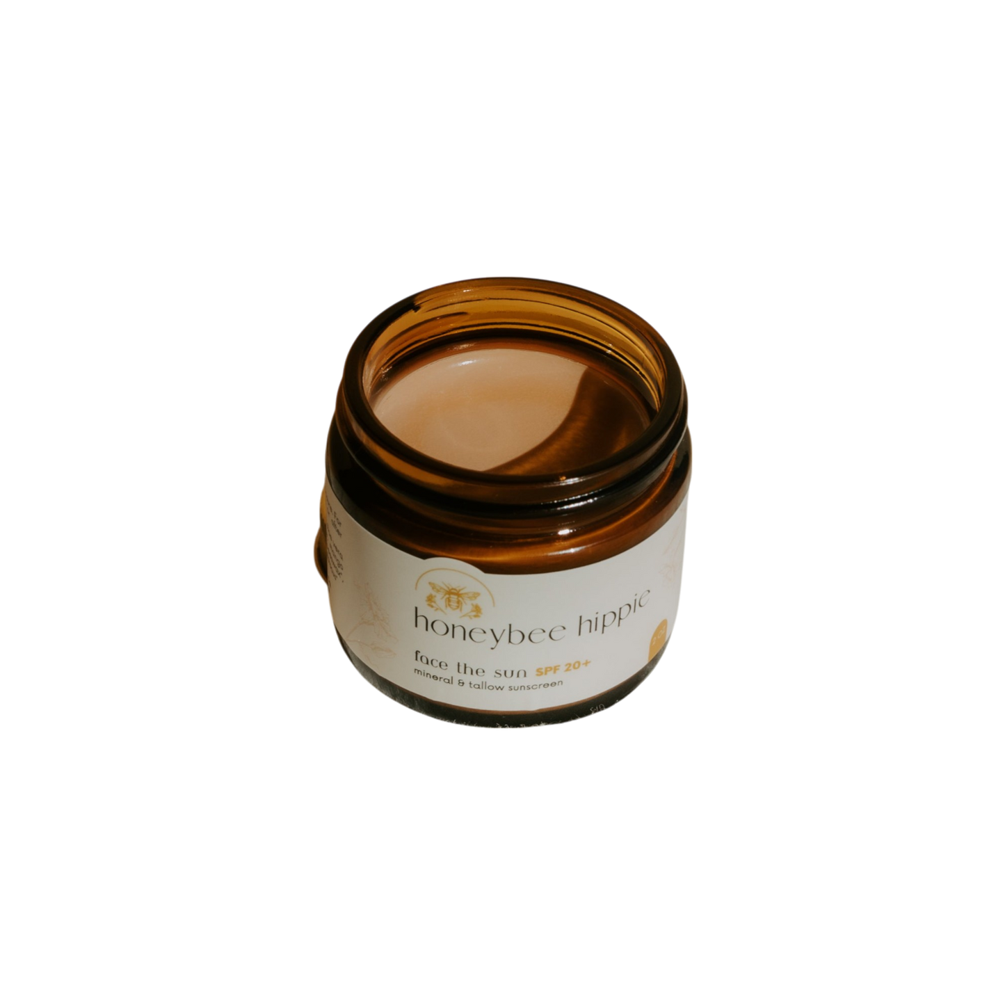 A brown glass jar labeled "Honeybee Hippie face the sun - herbal tinted mineral & tallow skin protection" with a creamy formula, offering natural UV defense and antioxidants, is photographed against a black background.