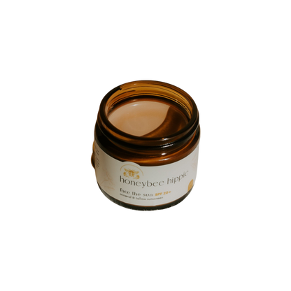 A brown glass jar labeled "Honeybee Hippie face the sun - herbal tinted mineral & tallow skin protection" with a creamy formula, offering natural UV defense and antioxidants, is photographed against a black background.