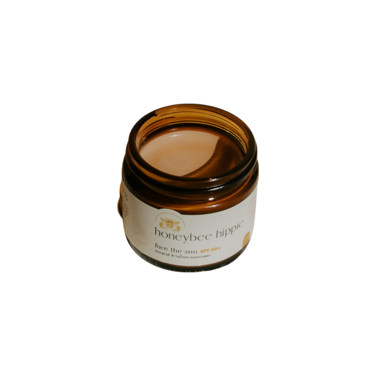 A brown glass jar labeled "Honeybee Hippie face the sun - herbal tinted mineral & tallow skin protection" with a creamy formula, offering natural UV defense and antioxidants, is photographed against a black background.