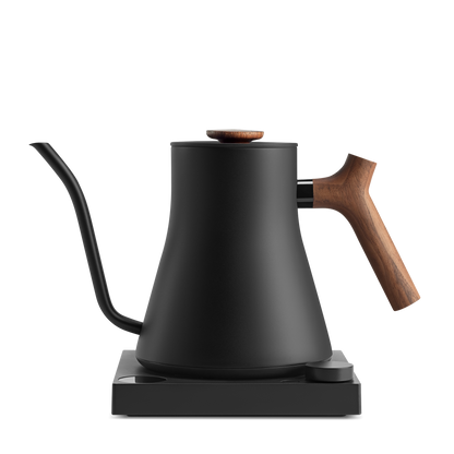 A sleek black pour-over kettle with a gooseneck spout and a wooden handle, the Stagg EKG Pro Electric Kettle from Fellow Wholesale sits on a matching black base. The design is minimalist and modern, combining metal and wood elements, and features customizable brew settings for the perfect cup every time.