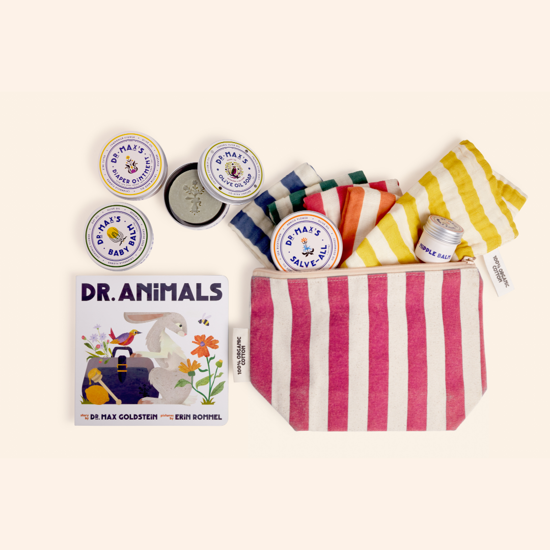 A flat lay featuring the New Parent Gift Box by Dr. Max's, including a striped pink and white pouch, striped baby clothes, essentials like tins and tubes of diaper ointment, and the children's book "Dr. Animals.