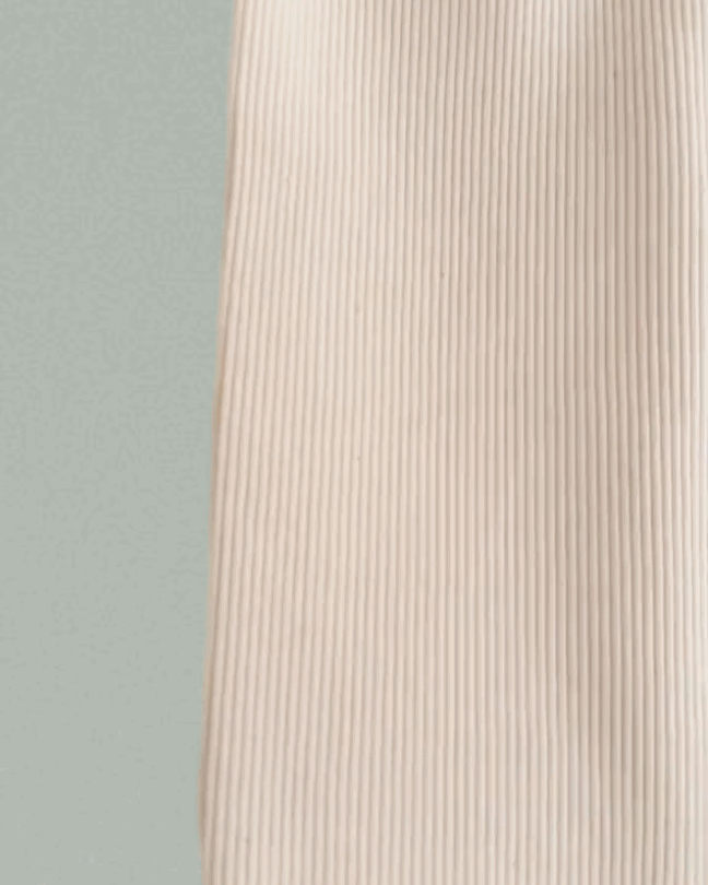 A close-up of the beige, ribbed FAVORIS rib pant by cabane childrenswear, made from natural cotton with vertical lines, set against a pale green background.