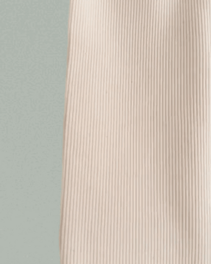 A close-up of the beige, ribbed FAVORIS rib pant by cabane childrenswear, made from natural cotton with vertical lines, set against a pale green background.