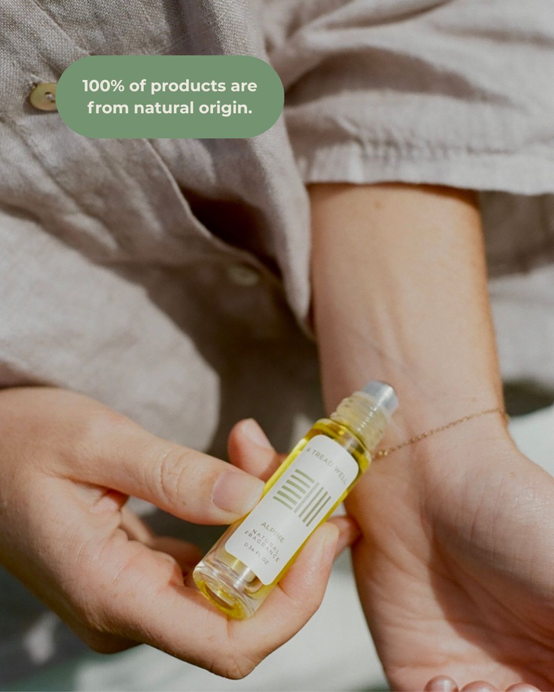 A person in a beige long-sleeve shirt applies & Tread Well Natural Fragrance - Alpine roll-on to their wrist. Text above reads, "100% of products are from natural origin.