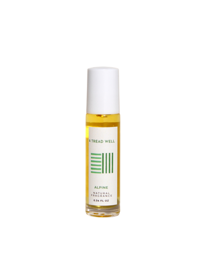 A small glass bottle with a white cap and roll-on applicator contains yellow "Natural Fragrance - Alpine" by & Tread Well (0.34 FL OZ), featuring organic essential oils and a label with green design elements.