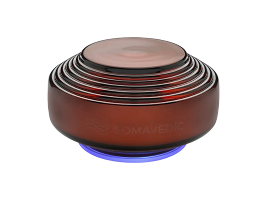 Amber by Somavedic USA is a round, dark amber device with ribbed rings on top and a glowing blue base, bearing “SOMAVEDIC” on its side. It’s designed for EMF mitigation and protection against 5G effects.