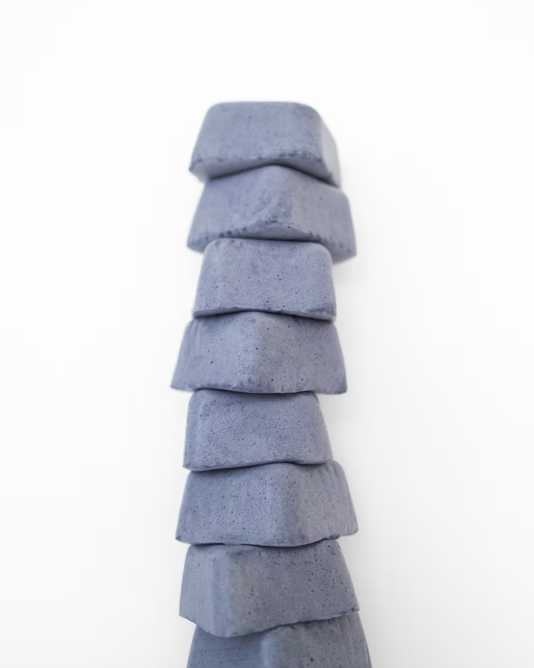 A stack of eight blue-gray blocks stands tall against a white background, evoking the calm strength found in Super Mallows' Beauty Mallow Super Mallow 8-pack—a glow-boosting treat with pearl powder for radiant skin.