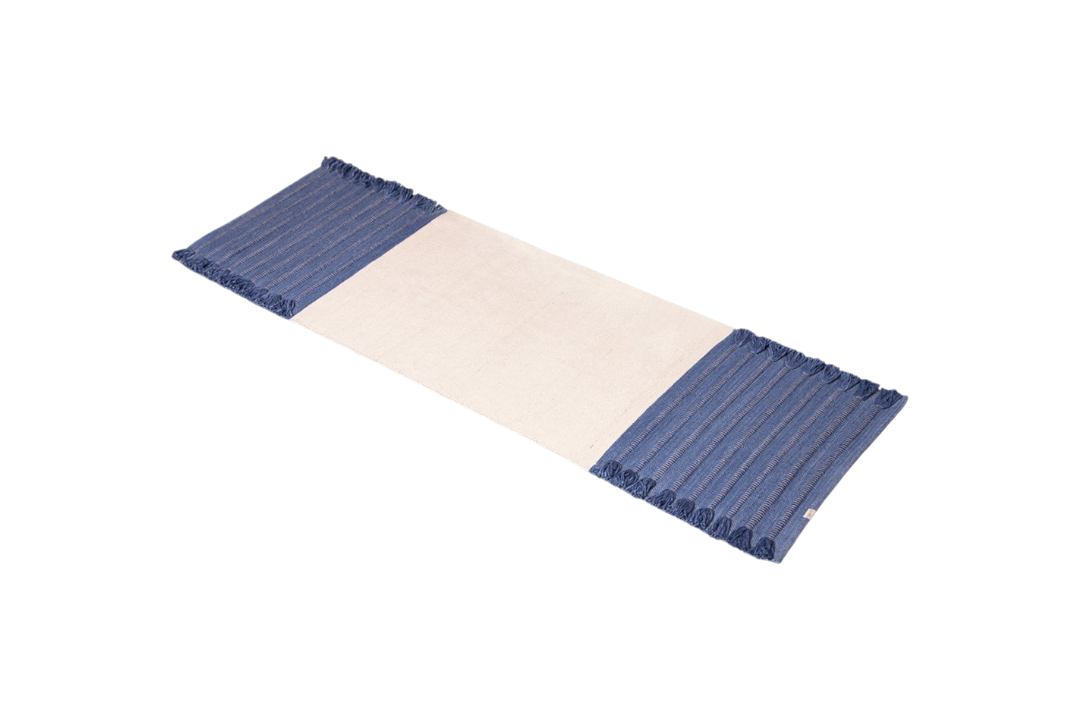 An organic cotton yoga mat by Bennd Yoga, named the Indigo Ayurvedic Yoga Mat, incorporates a beige center with blue-striped fringed edges.