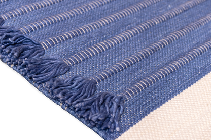 A close-up of the Bennd Yoga Indigo Ayurvedic Yoga Mat reveals fringe tassels along the edges, horizontal stripes, and visible stitching. Set against a black background, this mat provides superior grip for your practice.