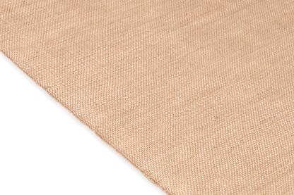 Close-up of the Harda Ayurvedic Yoga Mat's textured beige fabric, reminiscent of organic cotton and oriented diagonally. The weave is visible, displaying a simple and even pattern. The bottom left corner features a solid black background, providing contrast to the natural beauty of Bennd Yoga's textile.