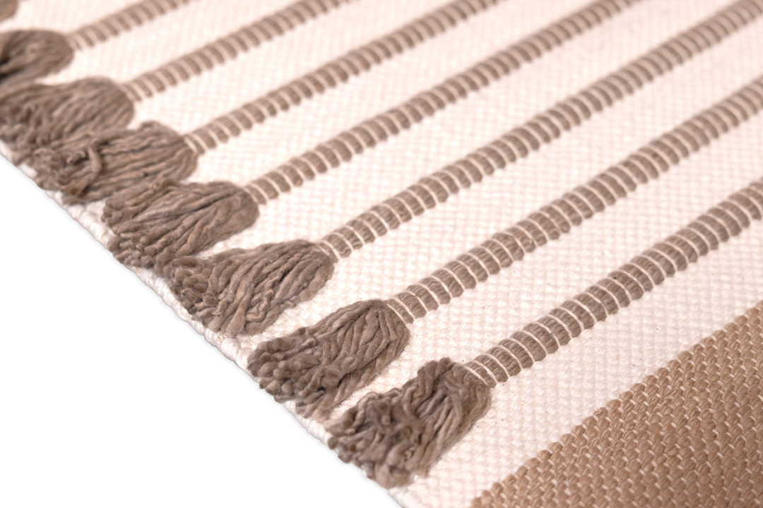 Close-up of a woven textile with alternating brown and white stripes, crafted from organic cotton. Rows of long, brown tassels align with each brown stripe, adding texture and depth to the design. The solid black background highlights the intricate details, reminiscent of Bennd Yoga's Harda Ayurvedic Yoga Mat.