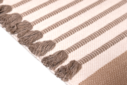 Close-up of a woven textile with alternating brown and white stripes, crafted from organic cotton. Rows of long, brown tassels align with each brown stripe, adding texture and depth to the design. The solid black background highlights the intricate details, reminiscent of Bennd Yoga's Harda Ayurvedic Yoga Mat.