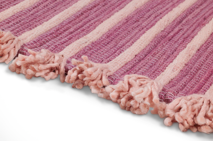 Experience a close-up of the Dark Harda and Sappan Wood Ayurvedic Yoga Mat from Bennd Yoga. This exquisite mat features a pink and white striped woven design with fringed edges. Its texture is soft and fluffy, crafted with thick yarn to create a cozy, tactile surface. When laid flat, it highlights intricate craftsmanship that enhances the inviting nature of your yoga practice.