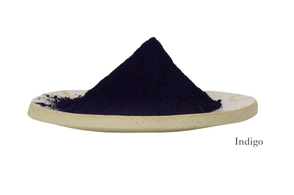 A mound of dark blue powder labeled "Indigo" sits on a beige ceramic dish against a white background, evocative of the deep hue featured in the Indigo Ayurvedic Yoga Mat by Bennd Yoga.