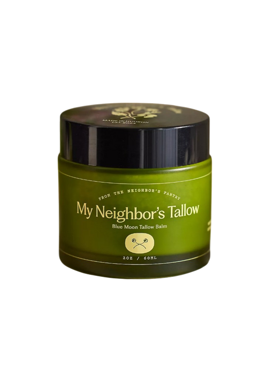 A green jar with a black lid labeled "Blue Moon Face Balm" by My Neighbor’s Tallow holds 2 oz (60 mL) of tallow-based face moisturizer with blue tansy oil. The dark label includes small icons and text.