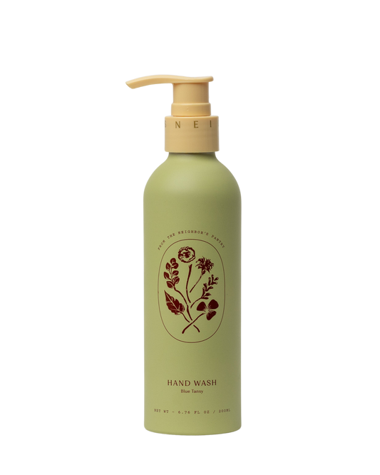 A green bottle of Blue Tansy Hand Wash by My Neighbor’s Tallow, featuring a beige pump dispenser, floral illustration, and the product name on the front.