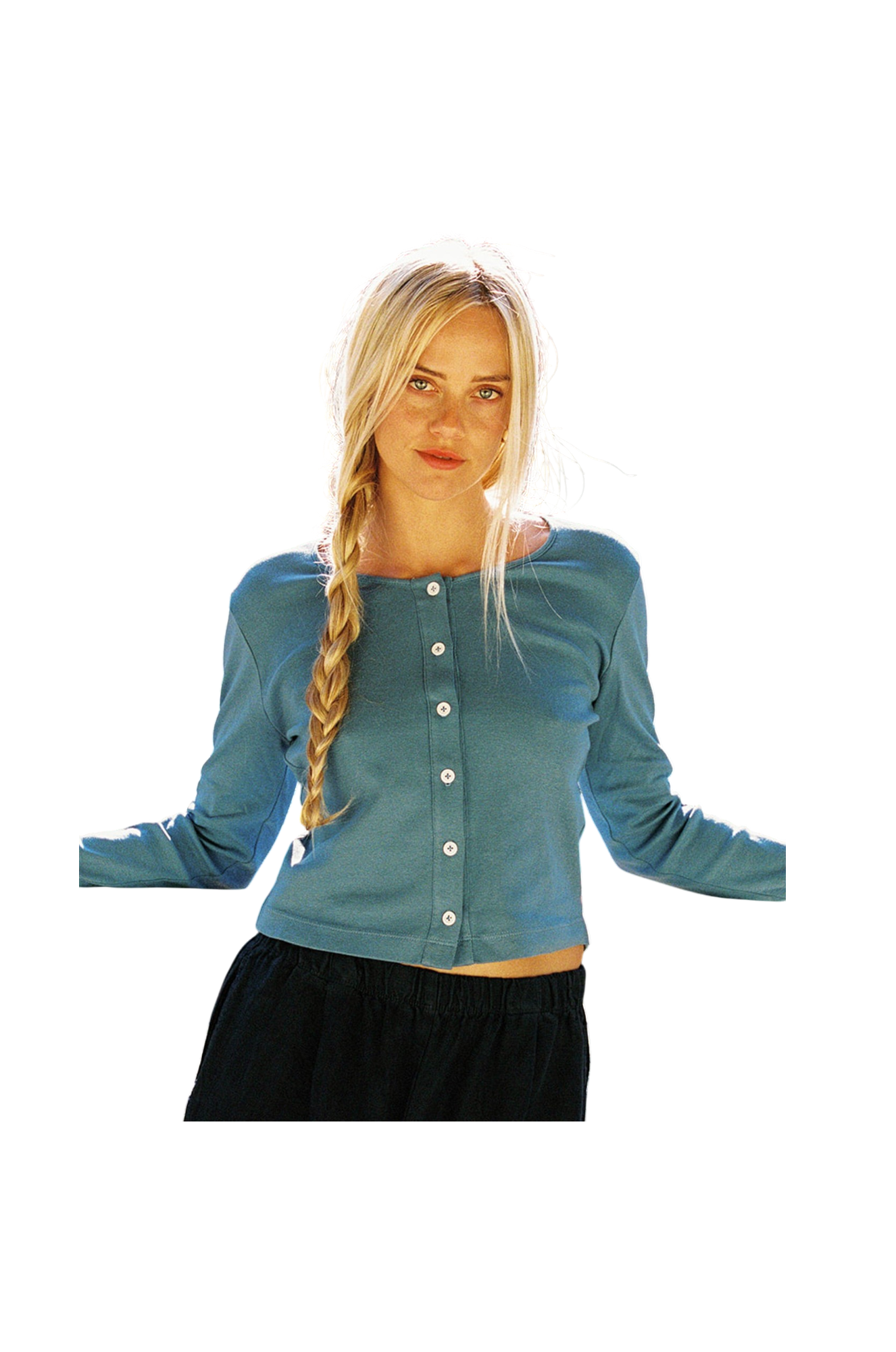 A person with long blonde hair in a braid wears the LA Relaxed Organic Rib Cardigan, featuring pearlescent buttons, paired with dark pants. They stand with arms slightly out to the sides against a completely blank background.