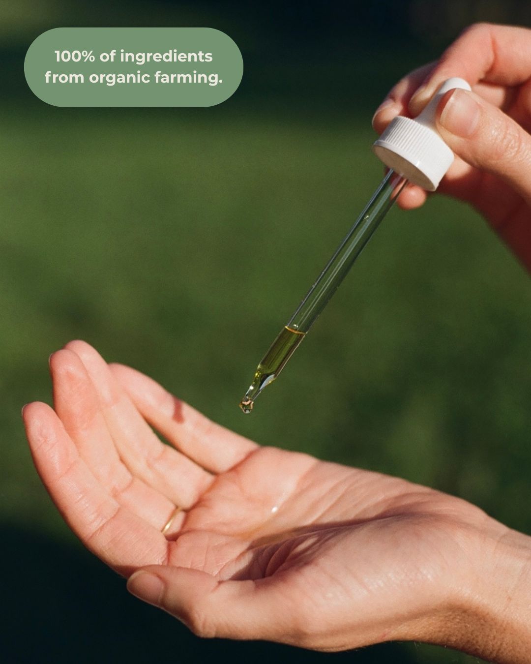 A hand uses a dropper to apply & Tread Well Body Oil onto an open palm. The image text says, "100% of ingredients from organic farming." A blurred green background highlights its hydration and skin barrier support.