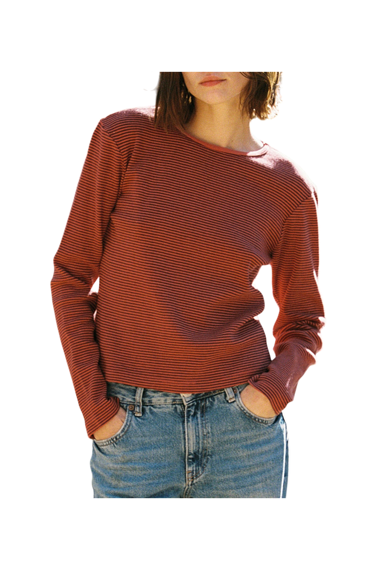 In front of a plain background, a person wears LA RELAXED's Organic Stripe Long Sleeve, featuring red and black stripes crafted from organic cotton, paired with blue jeans. Hands rest casually in pockets; face not visible.