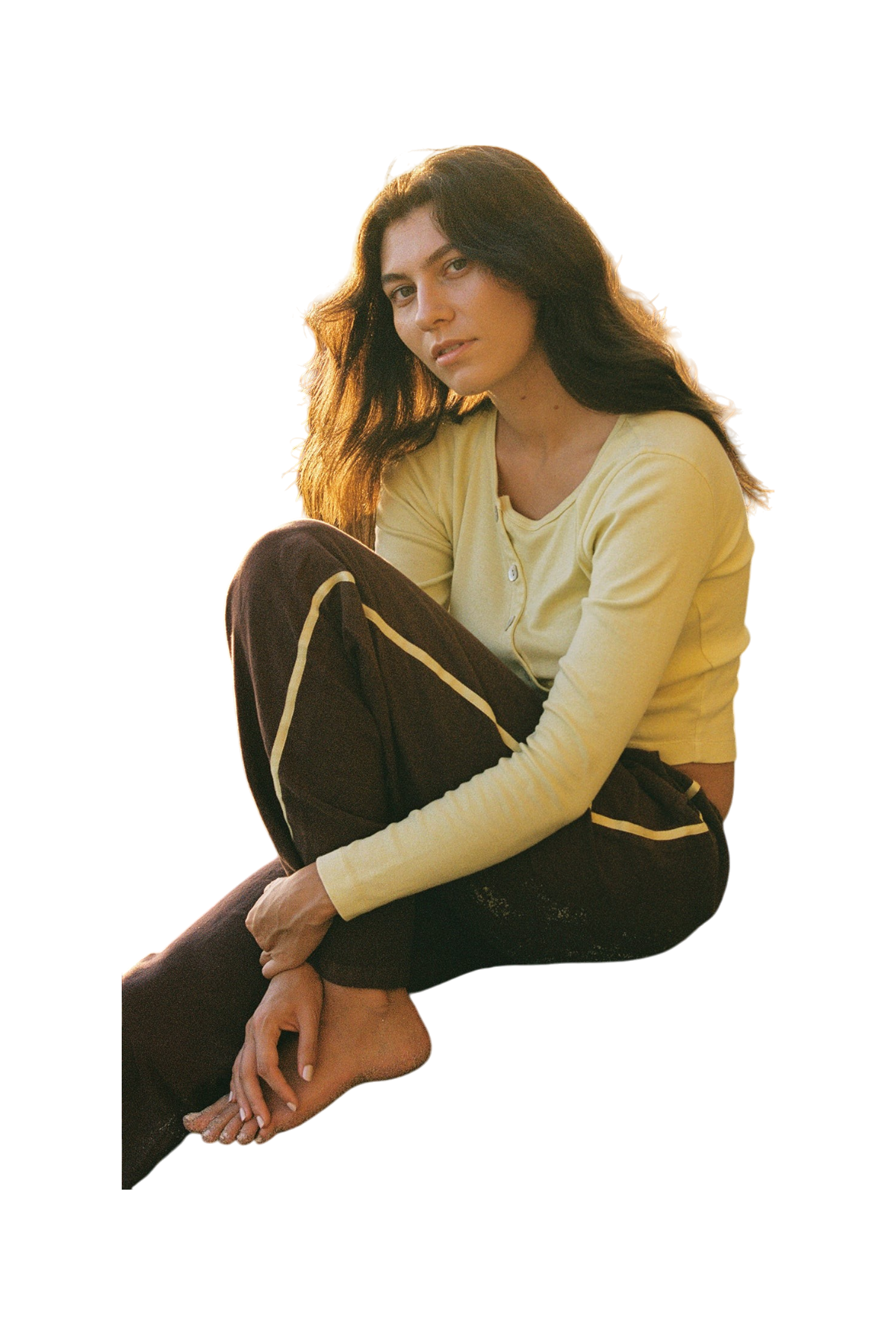 A young woman sits barefoot on the floor, thoughtfully gazing at the camera while wearing LA RELAXED’s Linen Track Pant.