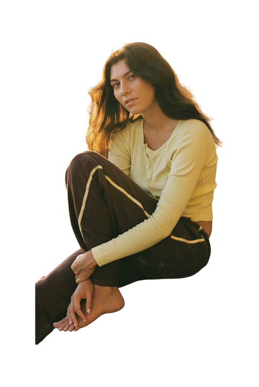 A young woman sits barefoot on the floor, thoughtfully gazing at the camera while wearing LA RELAXED’s Linen Track Pant.