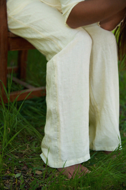 A person in LA RELAXED Linen Track Pant sits barefoot on a wooden chair outdoors, surrounded by green grass. Only their lower body and legs, highlighted by the pant’s relaxed drawstring waistband, are visible.