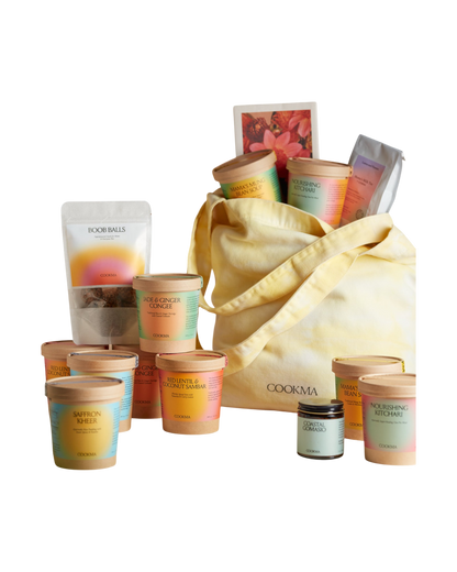The Cookma Mama Bundle features nourishing meals like Ayurvedic kitchari, colorful jars, tubs, pouches, recipe cards, and a small jar—all arranged around a yellow tote for holistic wellness.
