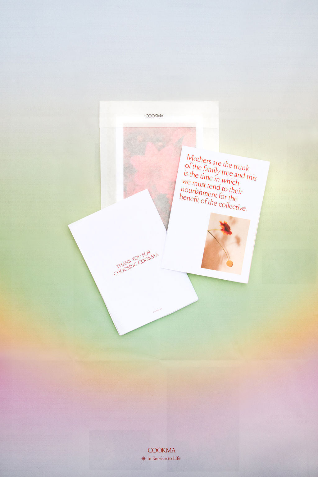 Three booklets from the Cookma Mama Bundle rest on a pastel, rainbow gradient background. One says, "THANK YOU FOR CHOOSING COOKMA." Another highlights mothers and family trees, all celebrating nourishing meals and postpartum restoration.